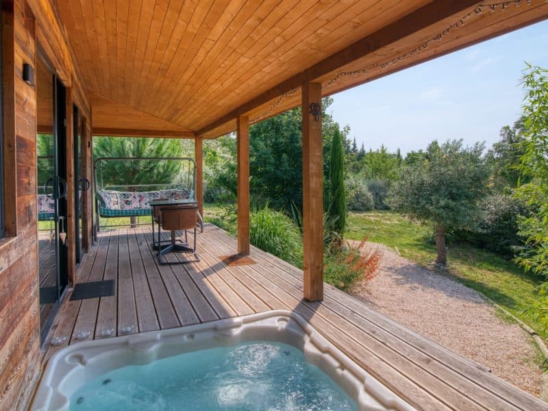 Cabane en bois avec terrasse, jacuzzi et vue sur un jardin verdoyant.