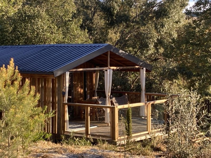 Cabane en bois avec terrasse, entourée de verdure et darbres.