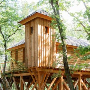 Cabane perchée en bois dans les arbres, entourée de verdure à Midi-Pyrénées.