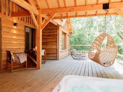 Cabane en bois perchée avec terrasse, hamac et jacuzzi, au cœur de la nature.