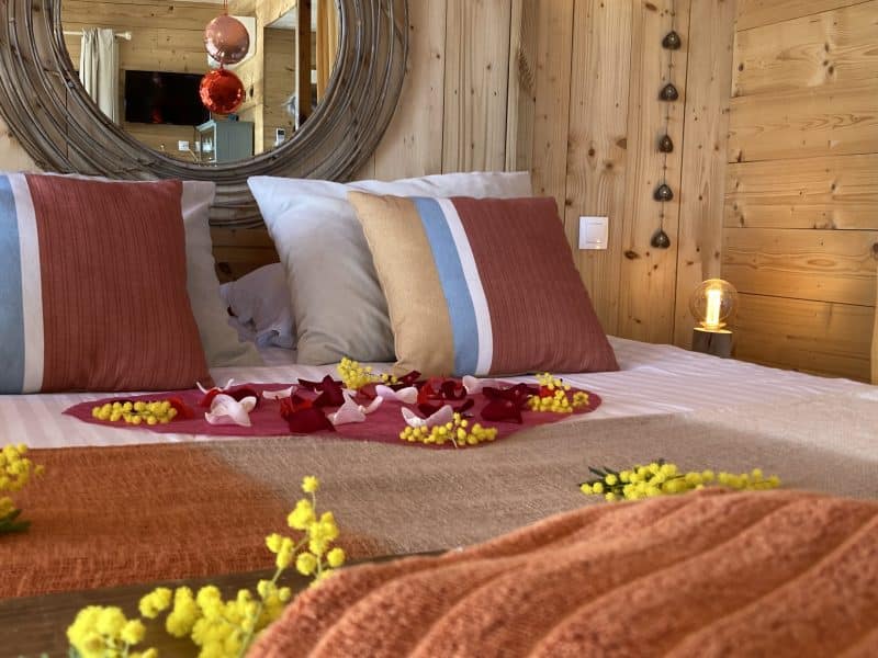 Chalet douillet avec lit décoré de pétales de fleurs et ambiance chaleureuse.