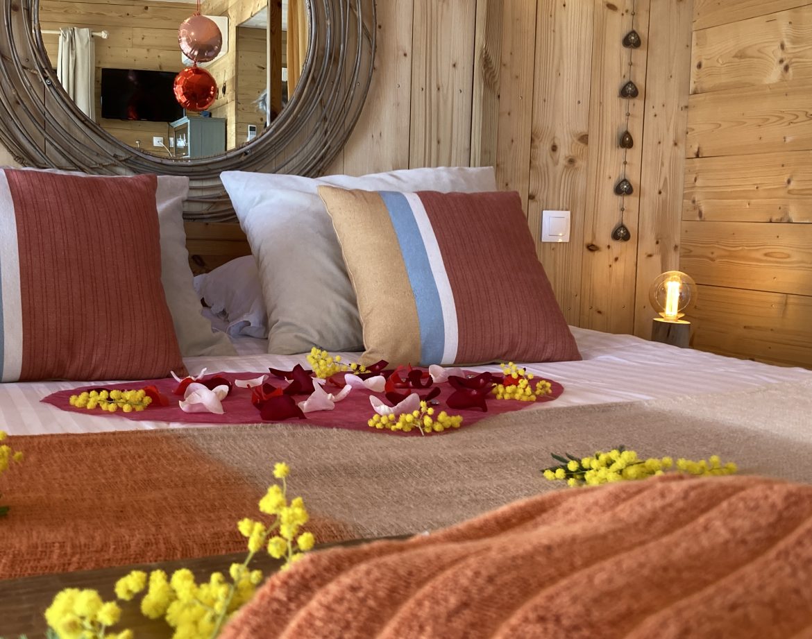 Chalet en bois cosy avec lit décoré de pétales de fleurs et ambiance chaleureuse.