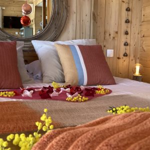 Chalet en bois cosy avec lit décoré de pétales de fleurs et ambiance chaleureuse.