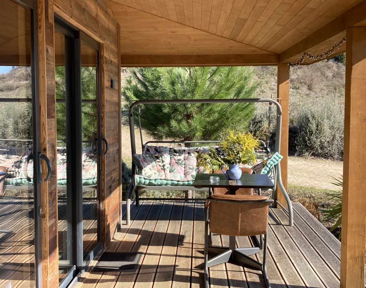 Cabane en bois avec terrasse, fauteuils confortables et vue sur la nature environnante.