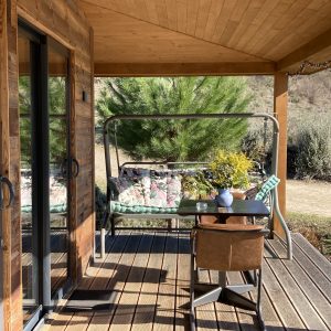 Cabane en bois avec terrasse, fauteuils confortables et vue sur la nature environnante.