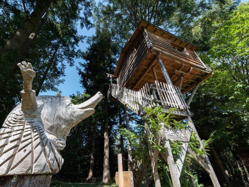 Cabane dans les arbres entourée de verdure, avec une sculpture en bois dun animal.