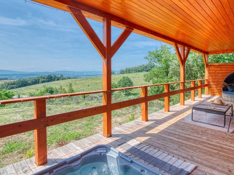 Chalet en bois avec terrasse, jacuzzi et vue panoramique sur la campagne.