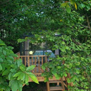 Cabane perchée en bois, nichée dans la verdure, avec une terrasse accueillante.