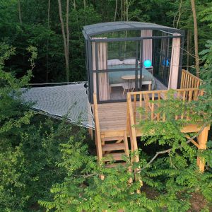 Cabane perchée dans les arbres, avec un espace vitré et une terrasse en bois.