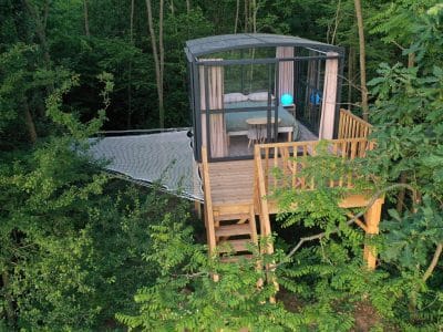 Cabane perchée dans les arbres, avec un espace vitré et une terrasse en bois.
