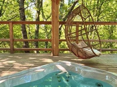 Hébergement insolite en Midi-Pyrénées avec jacuzzi et hamac en bois, entouré de verdure.