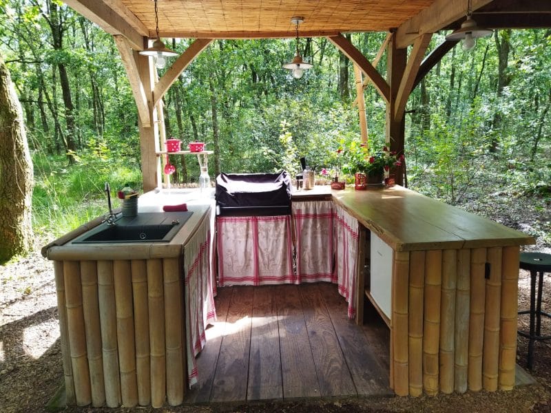 Cuisine en plein air en bois, entourée de verdure, idéale pour des séjours nature.