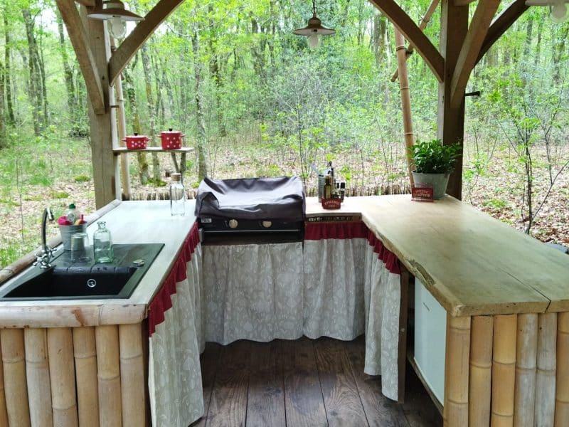 Cuisine extérieure en bois avec barbecue, entourée de verdure apaisante.