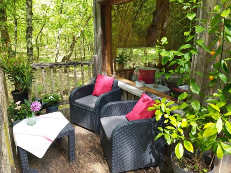 Chalet en bois avec terrasse, fauteuils confortables et verdure environnante.