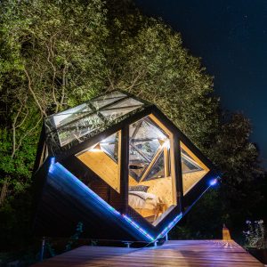 Cabane en verre suspendue sous les étoiles, entourée de verdure apaisante.