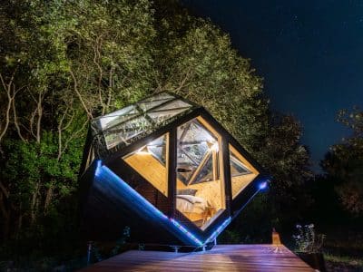 Cabane en verre suspendue sous les étoiles, entourée de verdure apaisante.