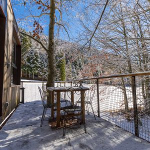 Cabane en bois avec terrasse, entourée de neige et de paysages forestiers.