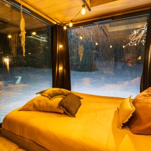 Chambre cocooning en verre avec vue sur la neige, ambiance chaleureuse et lumineuse.