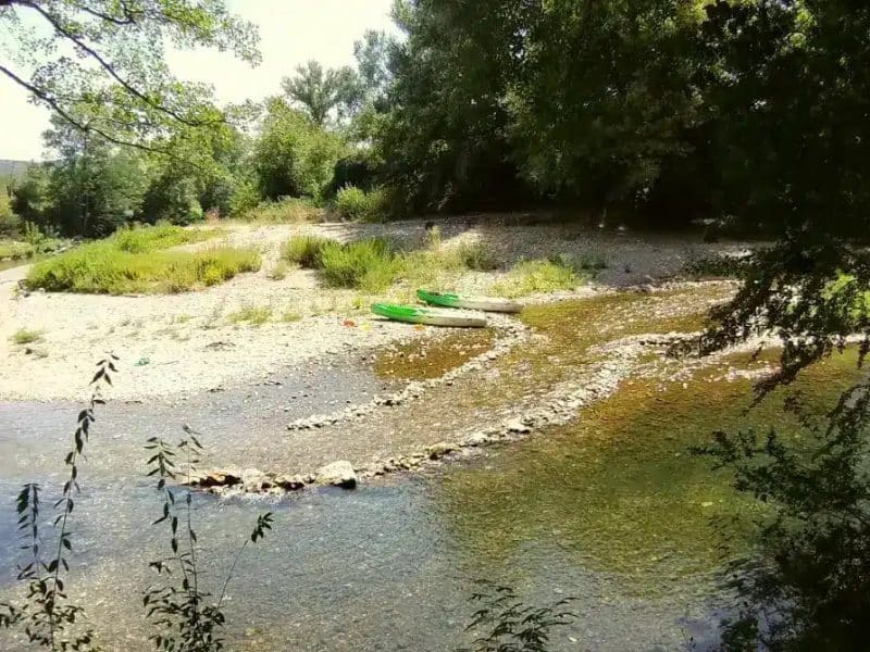 Hébergement en bord de rivière, avec des kayaks verts sur la berge.