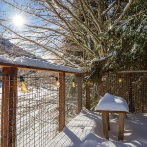 Cabane perchée en bois, entourée de neige et de lumière naturelle, offrant une vue paisible.
