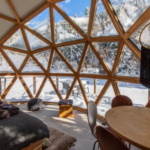 Dôme géodésique en bois, avec vue panoramique sur la neige et un intérieur chaleureux.
