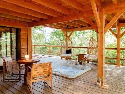 Cabane en bois avec jacuzzi sur la terrasse, entourée de verdure.