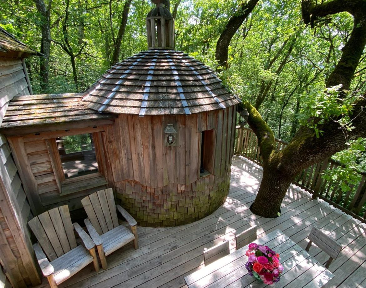 Cabane en bois dans les arbres, avec terrasse en bois et vue sur la nature verdoyante.