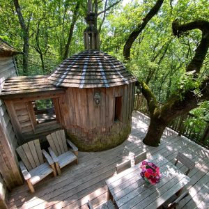 Cabane en bois dans les arbres, avec terrasse en bois et vue sur la nature verdoyante.