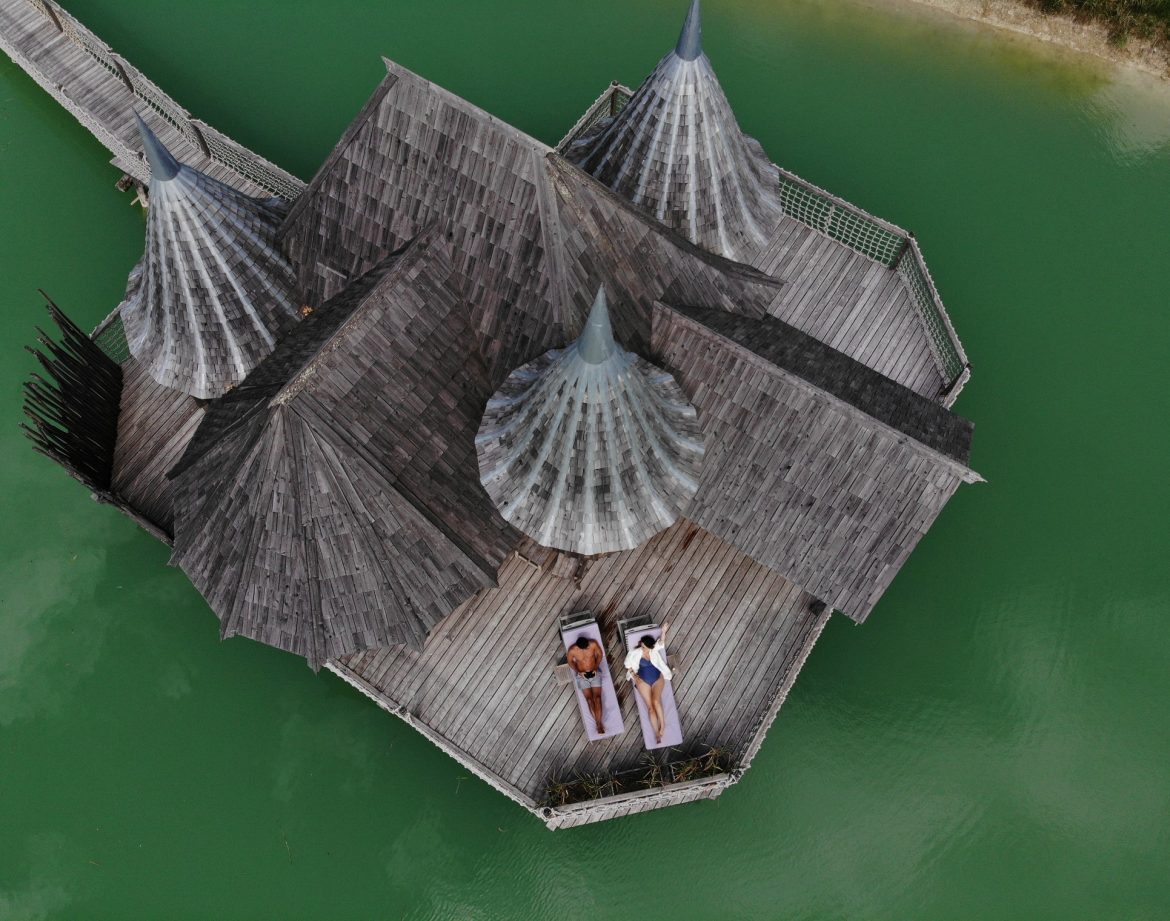 Hébergement insolite en Aquitaine : cabanes en bois sur pilotis au bord dun lac turquoise.