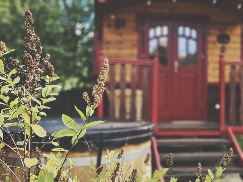 Roulotte en bois avec un jacuzzi en bois, entourée de verdure à Midi-Pyrénées.
