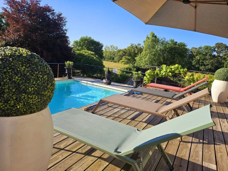 Villa avec piscine, chaises longues sur la terrasse entourée de verdure.