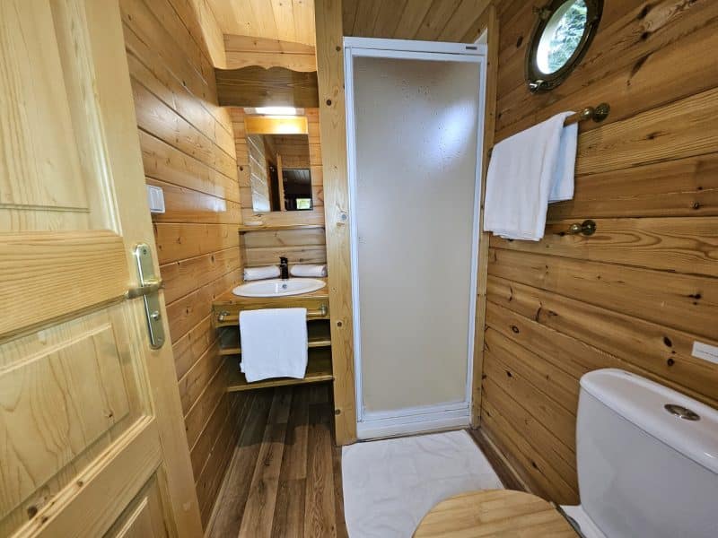Salle de bain en bois dans un chalet, avec douche et lavabo lumineux.