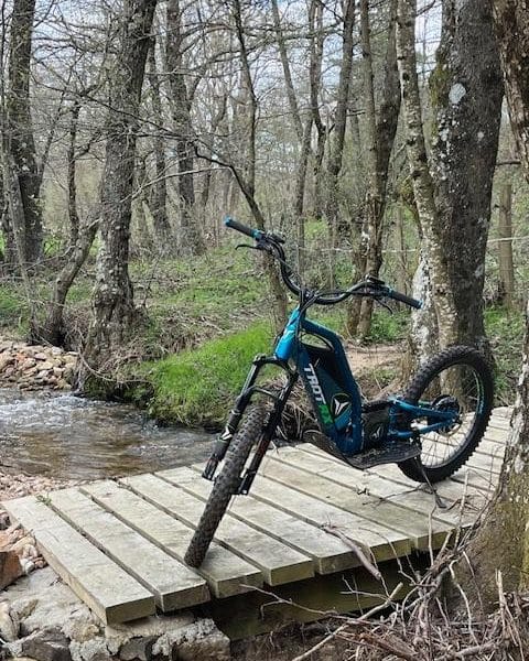 Vélo tout terrain posé sur un pont en bois près dun ruisseau, dans un cadre naturel.