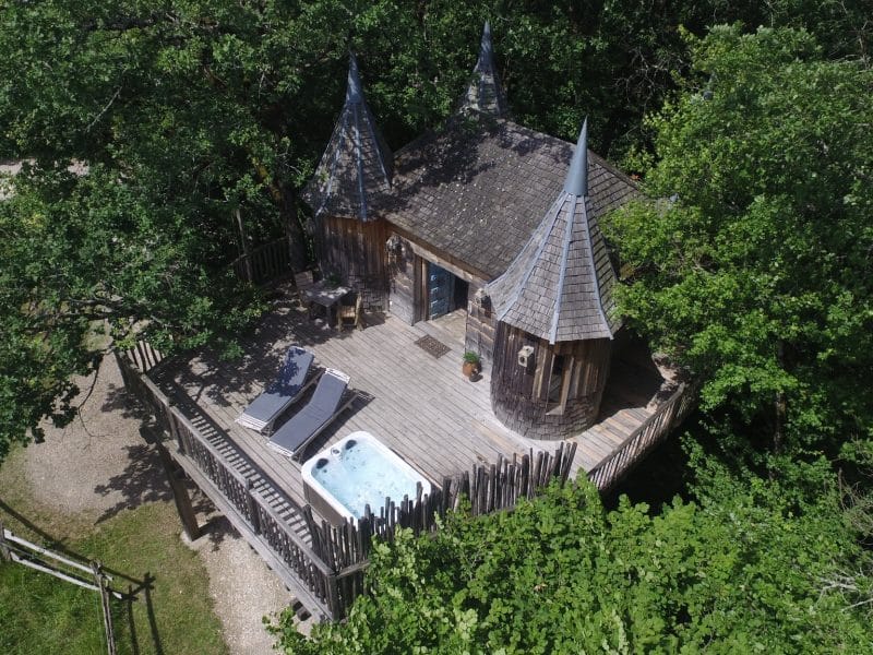 Cabane perchée en Aquitaine avec terrasse en bois et jacuzzi entouré darbres.