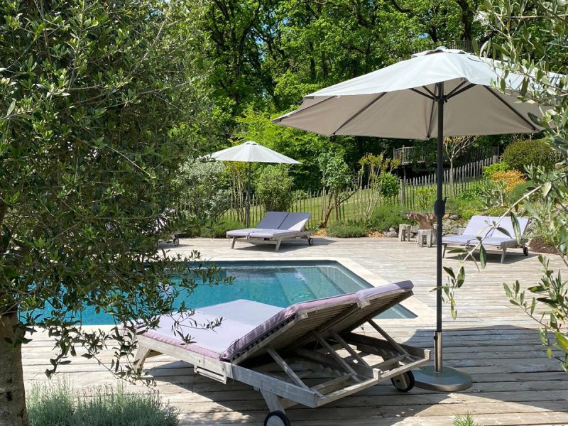 Chambres dhôtes avec piscine, chaises longues sous parasols au milieu de la verdure.