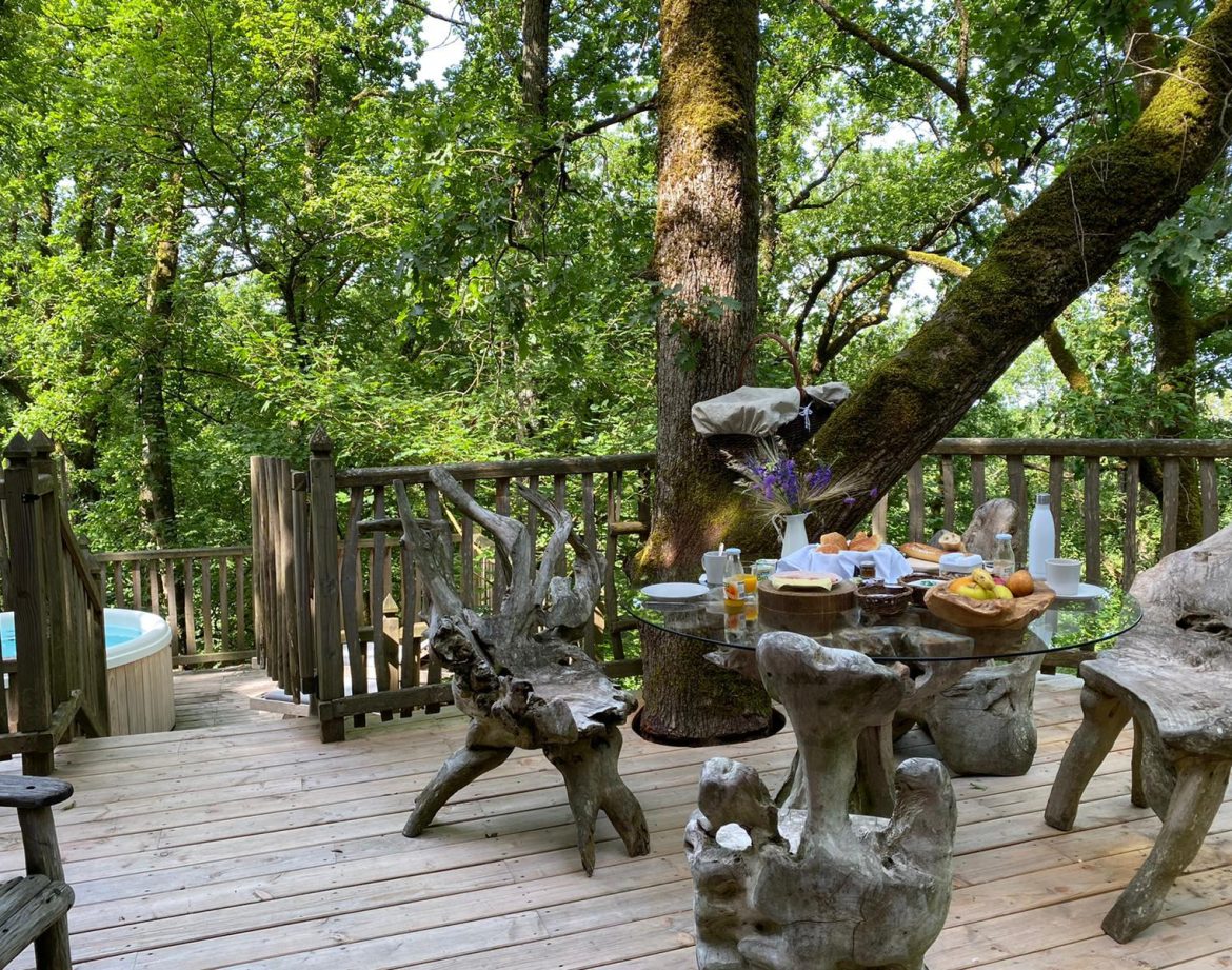 Cabane perchée en Aquitaine, avec terrasse en bois et jacuzzi au milieu des arbres.