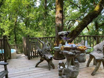 Cabane perchée en Aquitaine, avec terrasse en bois et jacuzzi au milieu des arbres.
