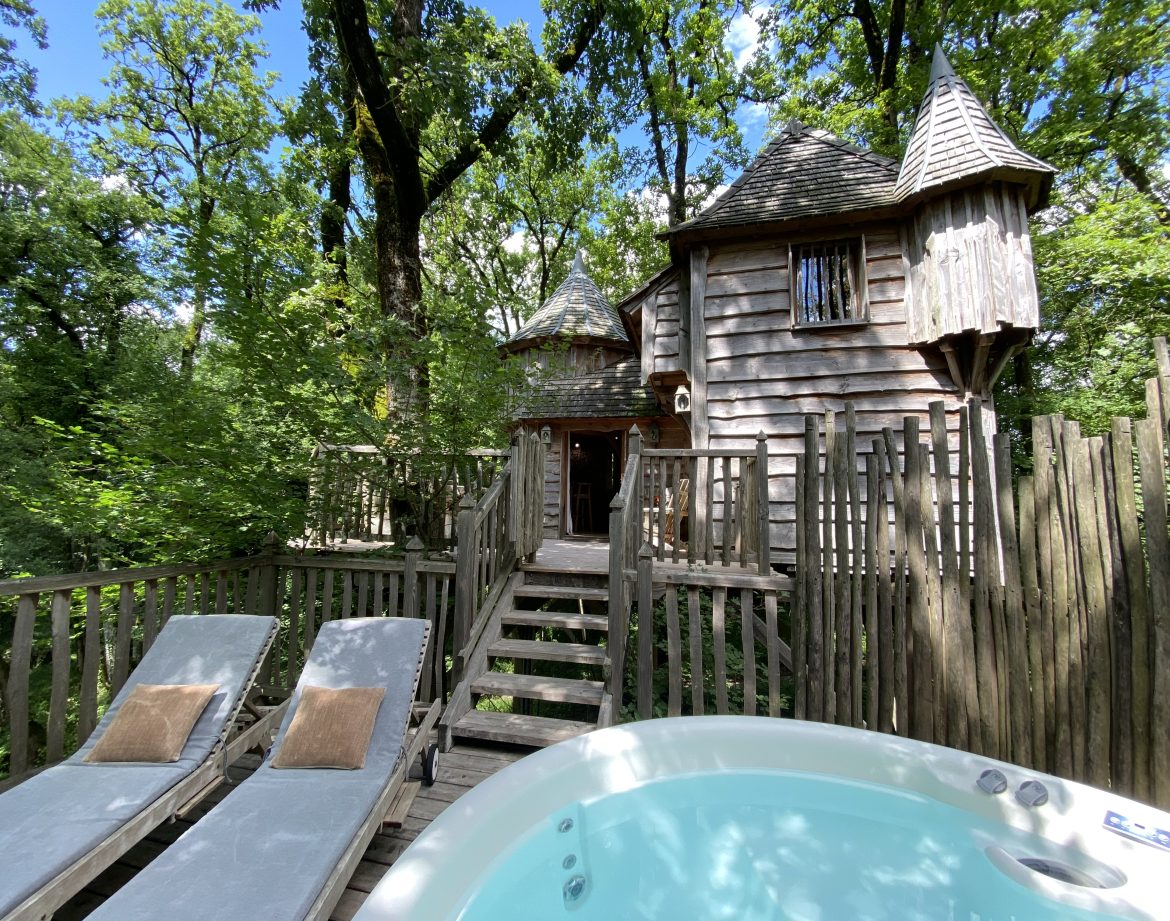 Cabane perchée en bois avec jacuzzi, entourée darbres verdoyants en Aquitaine.