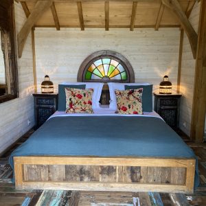 Chalet en bois avec lit king-size et fenêtres colorées, ambiance chaleureuse.