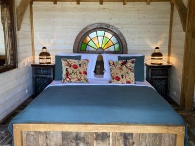 Chalet en bois avec lit king-size et fenêtres colorées, ambiance chaleureuse.