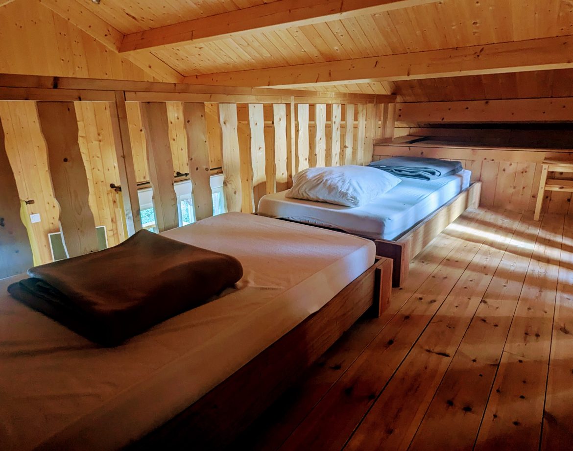 Chalet en bois avec lits simples, ambiance chaleureuse et lumineuse en Auvergne-Rhône-Alpes.