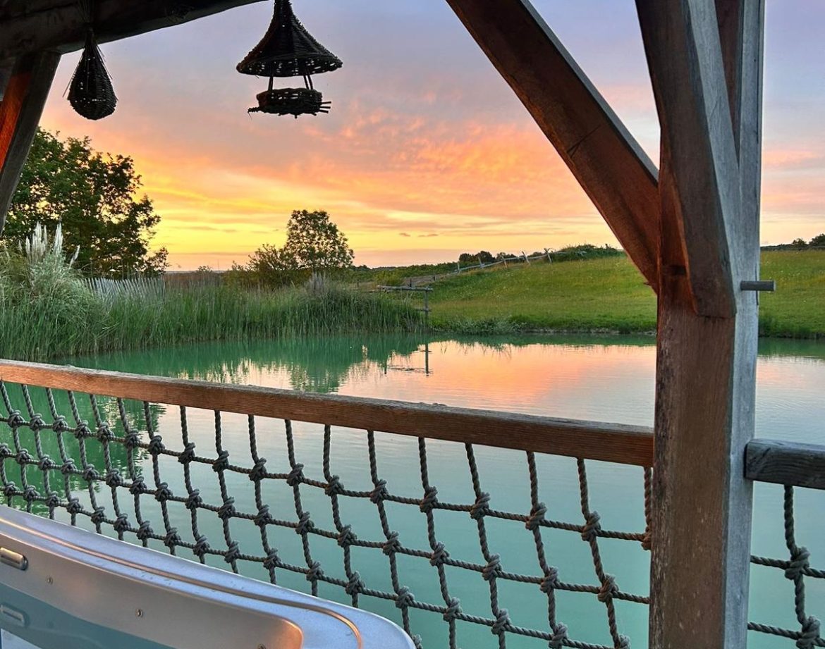 Hébergement insolite en Aquitaine avec jacuzzi, vue sur un lac au coucher du soleil.