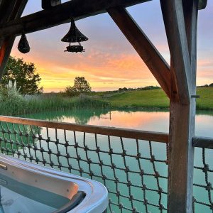 Hébergement insolite en Aquitaine avec jacuzzi, vue sur un lac au coucher du soleil.