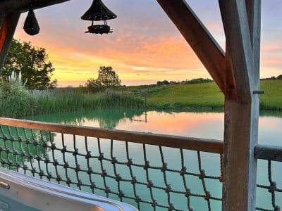 Hébergement insolite en Aquitaine avec jacuzzi, vue sur un lac au coucher du soleil.