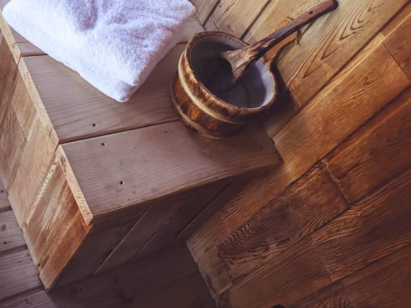 Sauna en bois avec serviette blanche et seau en bois pour une expérience relaxante.