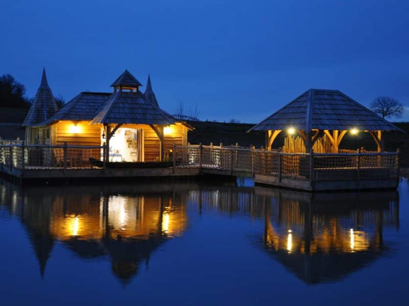 Hébergement insolite en Aquitaine : cabanes lumineuses sur leau, reflet magique au crépuscule.