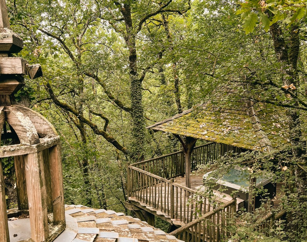 Cabane perchée en Aquitaine, entourée darbres verdoyants et dune terrasse en bois.