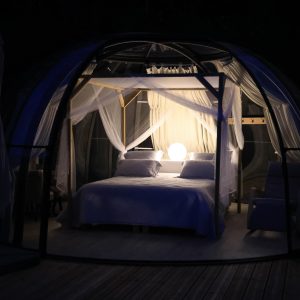Hébergement insolite en bulle transparente, lit romantique éclairé par une douce lumière.