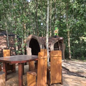 Hébergement insolite en cabane dans les arbres, avec table en bois et chaises rustiques.