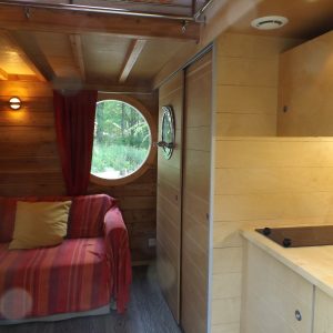 Hébergement insolite en Nouvelle-Aquitaine, intérieur bois avec fenêtre ronde et canapé coloré.